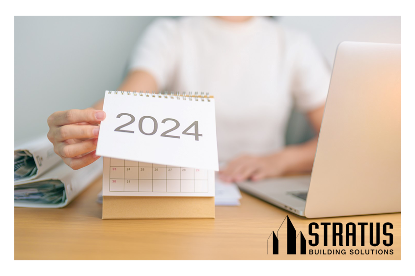 Torso of a Woman at a Table with a Laptop on it Reaching Out to Flip a Calendar with 2024 Printed on the Top Page